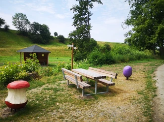 Sitzbank mit Tisch und Schutzhütte im Hintergrund, Rastplatz