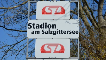 Stadion am Salzgittersee (15)_HD_16zu9.JPG Ein weißes Schild mit der schwarzen Aufschrift Stadion am Salzgittersee vor einem blauen Himmel.