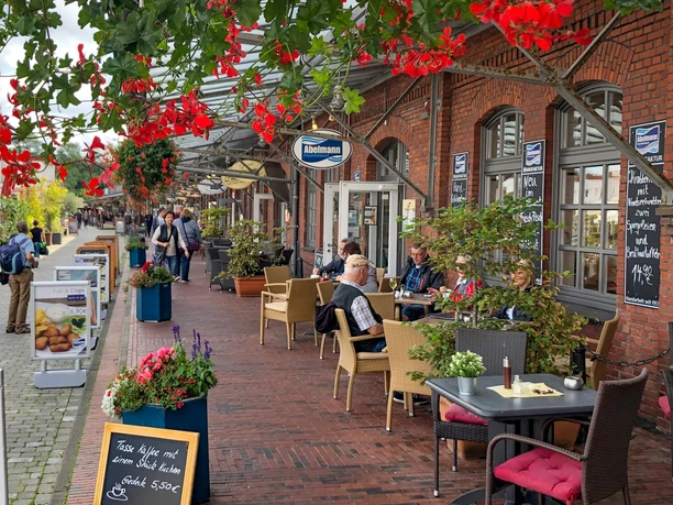 Schaufenster Fischereihafen IMG_0644 (c) Tanja Mehl_Erlebnis Bremerhaven_Ausschnitt.jpg Menschen sitzen vor rotem Backsteingebäude im Schaufenster Fischereihafen Bremerhaven und genießen Speisen.