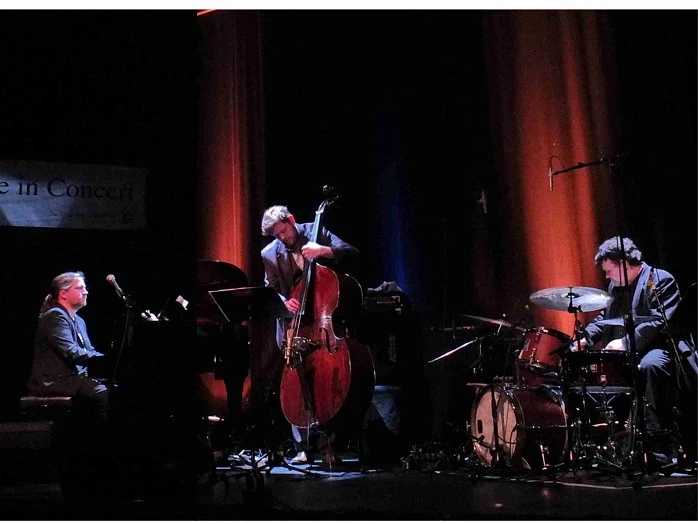 poppe_2025.jpg Drei Musiker spielen auf Bühne mit Klavier, Kontrabass und Schlagzeug in warmem Bühnenlicht.