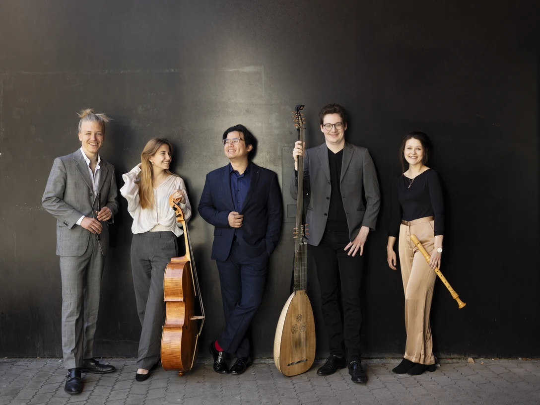 Ensemble Interchange © Astrid Ackermann Fünf Musiker stehen lächelnd vor einer dunklen Wand mit ihren Instrumenten.