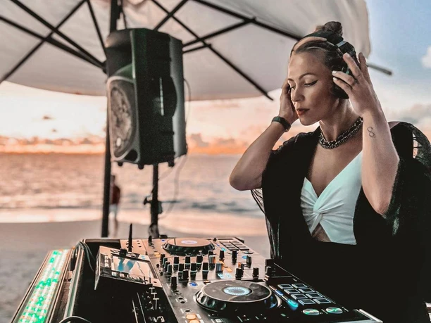 Soundshine Festival, DJane, Beach.jpg Eine DJane steht am Mischpult und hält ihre Kopfhörer fest