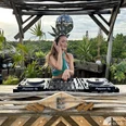 Soundshine Festival, DJane.jpg Eine DJane steht am Mischpult auf einer Bühne aus Holz, im Hintergrund stehen viele ParlmenA DJane stands at the mixing desk on a wooden stage, in the background are many parlums