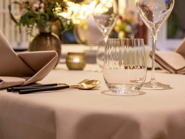 Sahila An elegantly laid table with golden cutlery and a golden vase with fresh flowers.