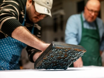 Blaudruck Workshop Zwei Männer arbeiten konzentriert beim Blaudruck mit einem verzierten Druckstempel auf Stoff.