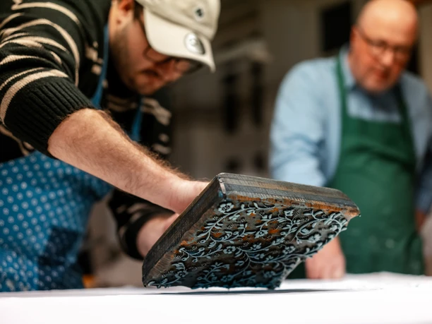 Blaudruck Workshop Zwei Männer arbeiten konzentriert beim Blaudruck mit einem verzierten Druckstempel auf Stoff.