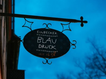 Metallschild des Einbecker Blaudrucks mit der Aufschrift „seit 1638“ vor blauem Abendhimmel