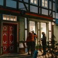 Blaudruck Workshop Menschen stehen abends vor dem Einbecker Blaudruckhaus mit Fachwerkfassade und Laternenlicht.People stand in front of the Einbeck blue print house with its half-timbered façade and lantern light in the evening.Folk står foran Einbecks blåtrykte hus med bindingsværksfacade og lanternelys om aftenen.Mensen staan 's avonds voor het blauwdrukhuis Einbeck met zijn vakwerkgevel en lantaarnlicht.