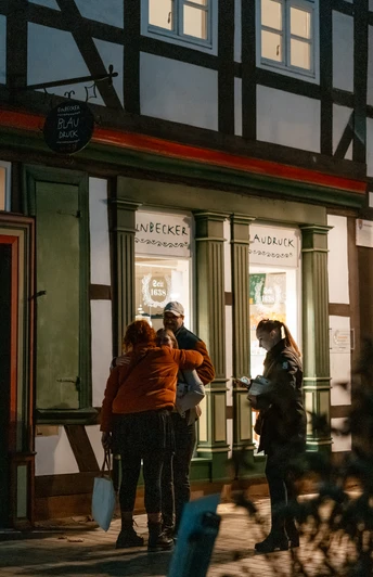 Blaudruck Workshop Menschen stehen abends vor dem Einbecker Blaudruckhaus mit Fachwerkfassade und Laternenlicht.People stand in front of the Einbeck blue print house with its half-timbered façade and lantern light in the evening.Folk står foran Einbecks blåtrykte hus med bindingsværksfacade og lanternelys om aftenen.Mensen staan 's avonds voor het blauwdrukhuis Einbeck met zijn vakwerkgevel en lantaarnlicht.