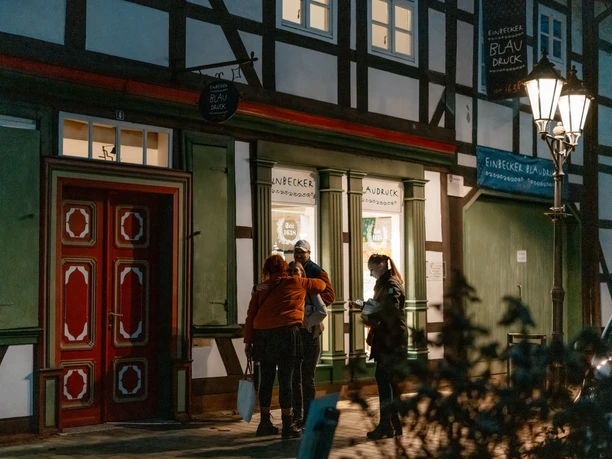 Blaudruck Workshop Menschen stehen abends vor dem Einbecker Blaudruckhaus mit Fachwerkfassade und Laternenlicht.
