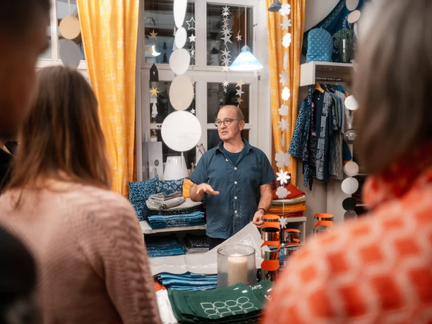 Blaudruck Workshop Ein Mann erklärt Teilnehmenden in einer Werkstatt die Blaudrucktechnik mit Stoffen und Mustern.