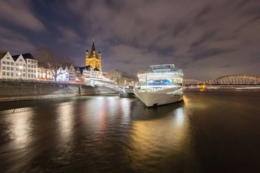 Weihnachtliche all-inclusive Abendfahrt Beleuchtetes Ausflugsschiff am nächtlichen Kölner Rheinufer mit Altstadt und Brücke