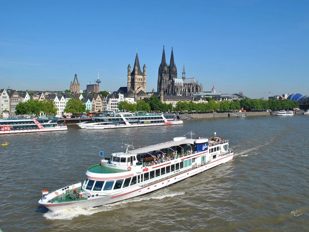 Panorama tour Cologne Rhine ship in front of Cologne's old town and cathedral under a blue sky.