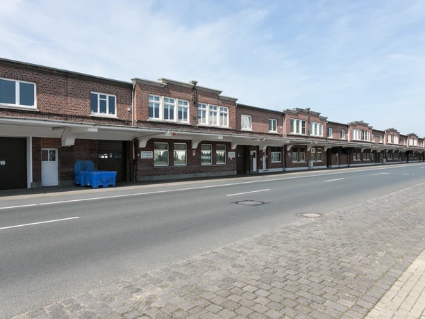 Halle XIV M3407 (c) Helmut Gross_Erlebnis Bremerhaven.jpg Lange Backsteinhalle mit weißem Vordach und großen Fenstern an einer ruhigen Straße in Bremerhaven.