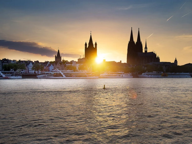 Lounge Abendfahrt Abendsonne über Köln mit Silhouetten von Dom, Altstadt und vorbeiliegenden Schiffen.