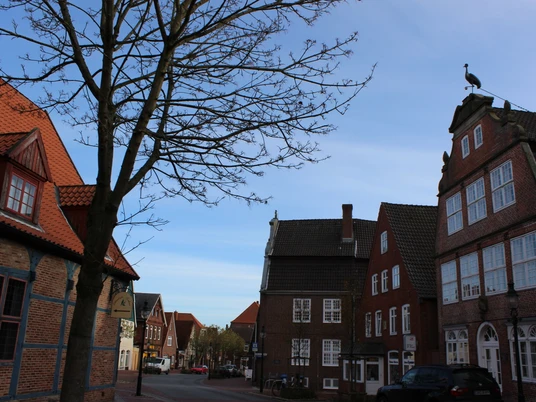 Kranichhaus Otterndorf © Stadt Otterndorf Straße mit alten Backsteinhäusern in Otterndorf. Auf einem Haus steht eine Storchenfigur.Street with old brick houses in Otterndorf. There is a stork figure on one of the houses.Gade med gamle murstenshuse i Otterndorf. Der er en storkefigur på et af husene.Straat met oude bakstenen huizen in Otterndorf. Op een van de huizen staat een ooievaarsfiguur.