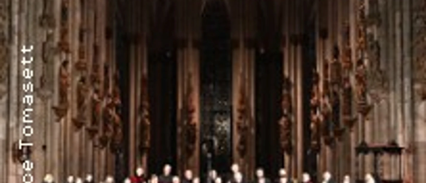 Chor und Orchester vor hoher gotischer Kulisse im Dom, umgeben von beleuchteten Säulen.