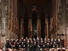 Chor und Orchester vor hoher gotischer Kulisse im Dom, umgeben von beleuchteten Säulen.