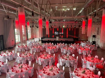 Dock² Eventlocation große Veranstaltungshalle in rotem Licht mit Bankettbestuhlung und Bühne mit RednerpultLarge event hall in red light with banquet seating and stage with lectern