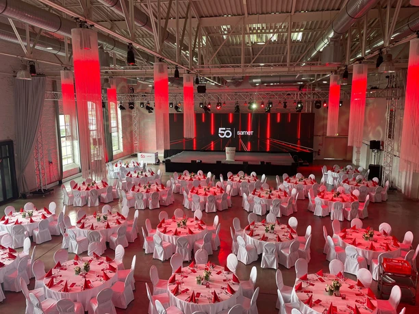 Dock² Eventlocation große Veranstaltungshalle in rotem Licht mit Bankettbestuhlung und Bühne mit Rednerpult