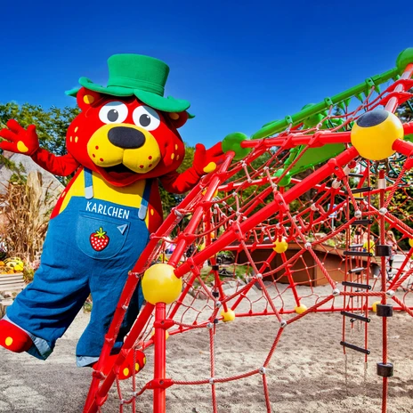 Red climbing frame in the shape of a strawberry at Karls Erlebnishof, next to it a disguised figure of Karlchen, the mascot.