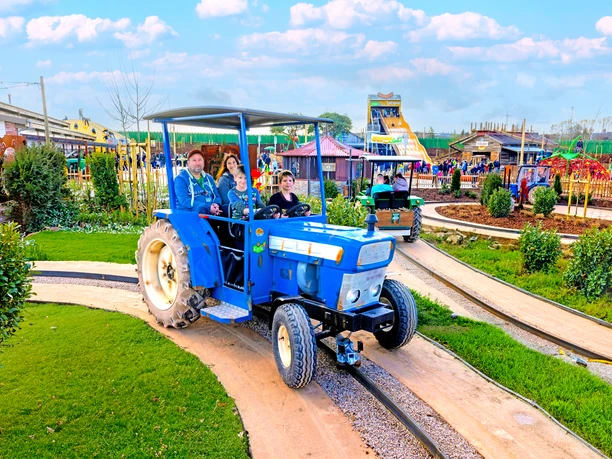Roześmiana rodzina siedząca w niebieskim traktorze na torze traktorów w Karls Adventure Village.