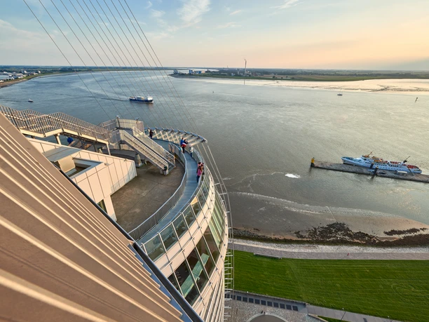 DSC_4104 (c) Anna Meurer_Erlebnis Bremerhaven.jpg Blick von der Aussichtsplattform SAiL City auf die Weser mit vorbeifahrenden Schiffen bei Sonnenlicht.