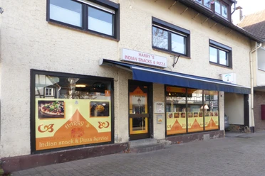 Front von einem Imbiss mit gelbem Fensterbild und blauem Dach über der Tür.