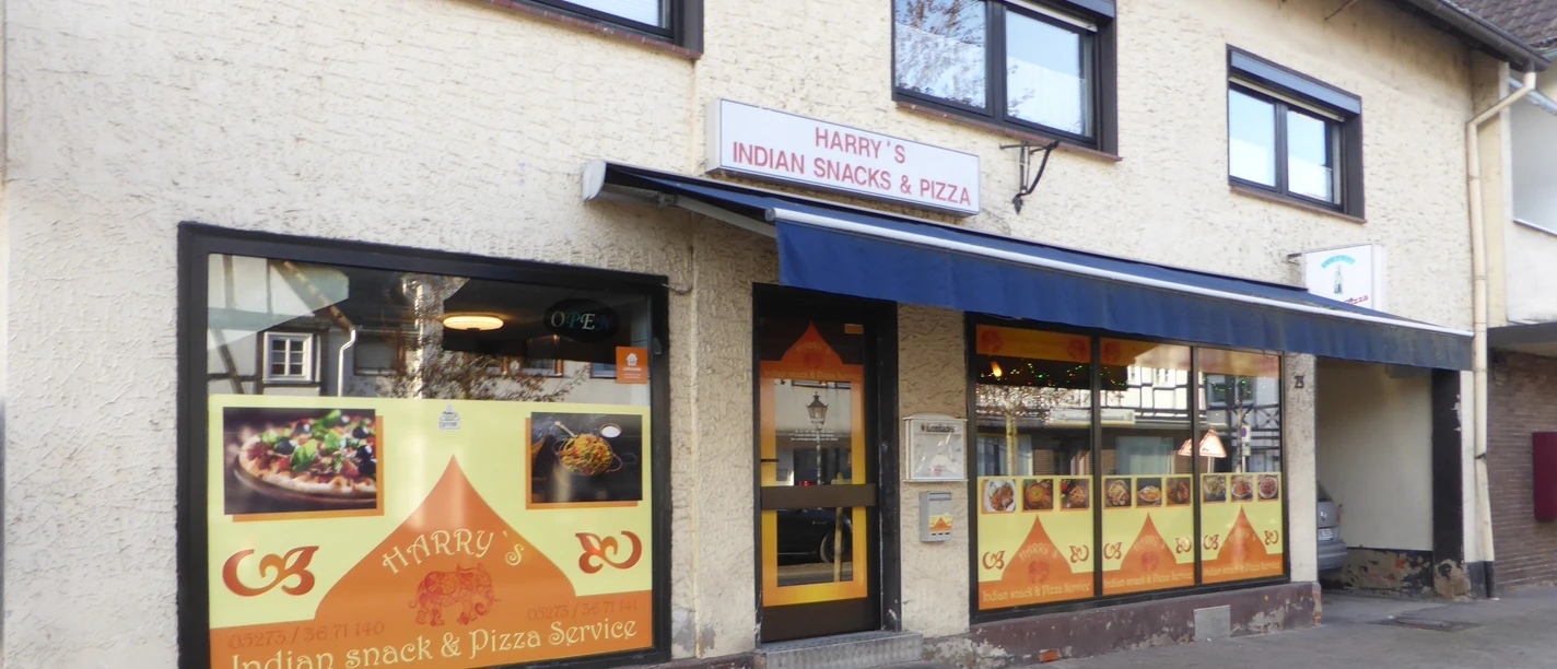 Front von einem Imbiss mit gelbem Fensterbild und blauem Dach über der Tür.