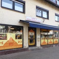 Harry`s Indian Snack & Pizza Front von einem Imbiss mit gelbem Fensterbild und blauem Dach über der Tür.