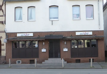 MyBar Fassade einer Stadtbar mit dunklen Fenstern, Markise und zentralem Eingang an der Straße.