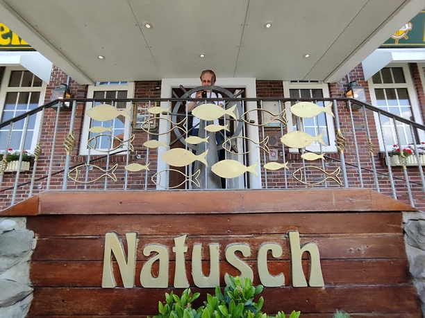 Mien Ogenblick 1305 (2) (c) Anja Härtel_Erlebnis Bremerhaven.jpg Eingang des Natusch Fischereihafen Restaurants mit goldener Fischgeländer-Verzierung und Holzschild