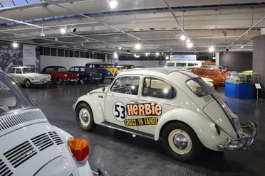 Innenraum mit alten VW-Autos. Vorn steht ein weißer Käfer mit Nummer 53.