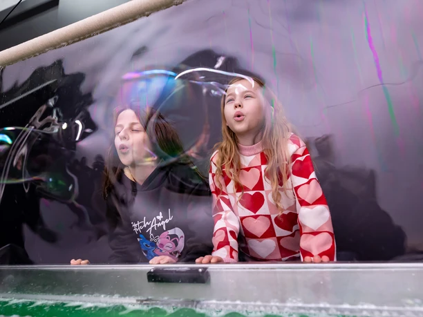 20_Jahre_phaeno_Pressemappe_ARudolph__6_.jpg Zwei Mädchen pusten gegen einen großen Seifenblasenfilm.