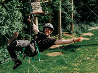 Frankfurt Climbing Forest Man hanging secured with arms outstretched in climbing park