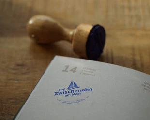 TANO-Nordsee-Reisepass-Stempel-Bad-Zwischenahn.jpg Holzstempel und blauer Abdruck mit Schriftzug „Bad Zwischenahn am Meer“ auf Nordseereisepassseite.