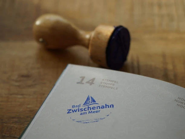 TANO-Nordsee-Reisepass-Stempel-Bad-Zwischenahn.jpg Holzstempel und blauer Abdruck mit Schriftzug „Bad Zwischenahn am Meer“ auf Nordseereisepassseite.
