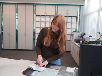 TANO-Nordsee-Reisepass-Abstempeln-Bad-Zwischenahn-am-Meer.jpg Frau stempelt einen Nordsee-Reisepass an einem Tresen der Tourist-Information in Bad Zwischenahn ab.