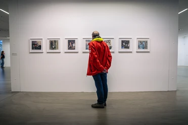 Ausstellung im Museum Ratingen Besucher in roter Jacke betrachtet Kunstwerke an einer weißen Wand im Museum Ratingen.