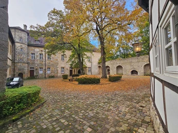 Steinernes Burghofensemble mit großem Baum, Pflaster und Torbögen an einem Herbsttag