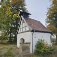Kleine weiße Fachwerkkapelle mit Glockenstuhl, umgeben von herbstlichen Bäumen.
