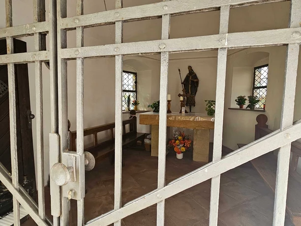 Blick durch Gitter in kleine Kapelle mit Altar, Statue, Bank und Blumen