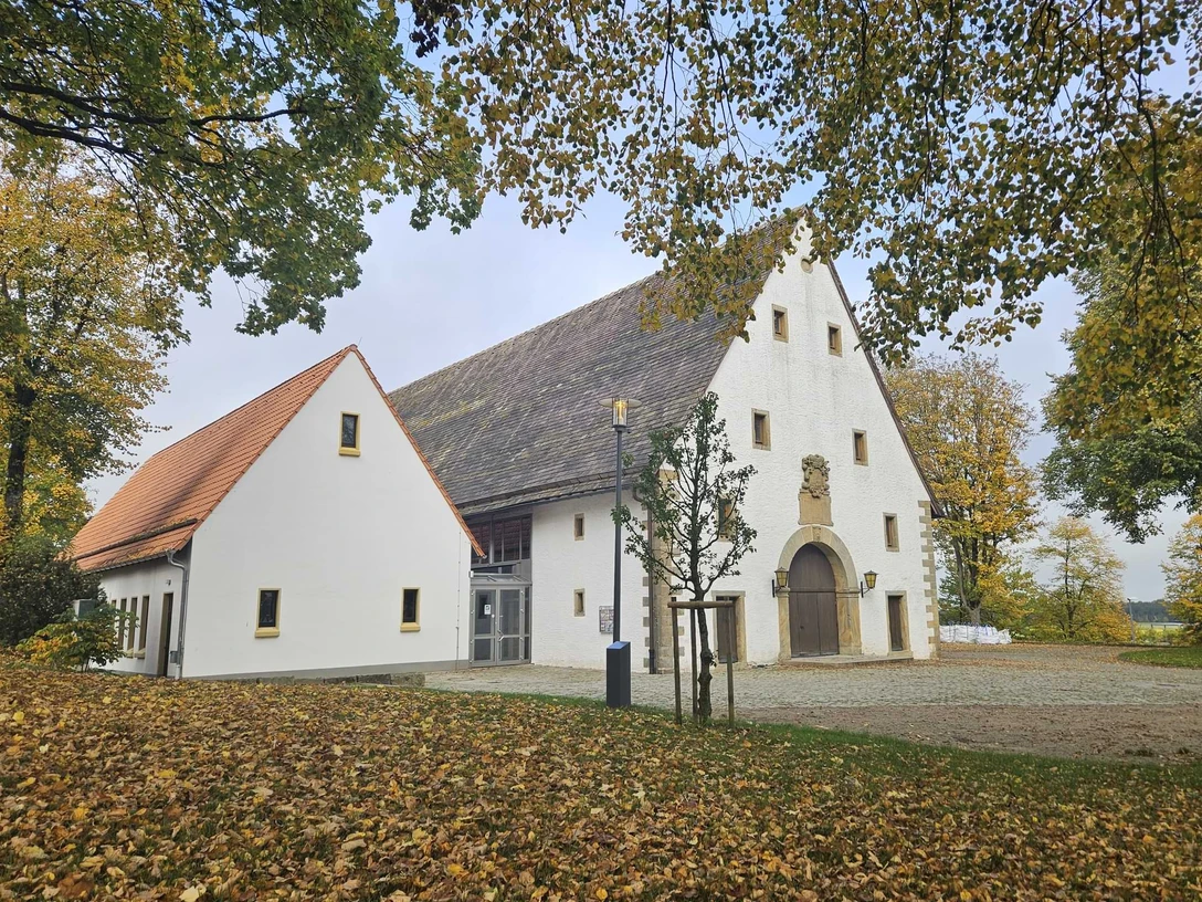 Dringenberg-Zehntscheune Weiße Zehntscheune mit hohem Giebel und Herbstlaub im Vordergrund.