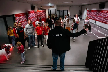 Stadionführung Eine Gruppe steht vor einem Mann und hört aufmerksam zu.