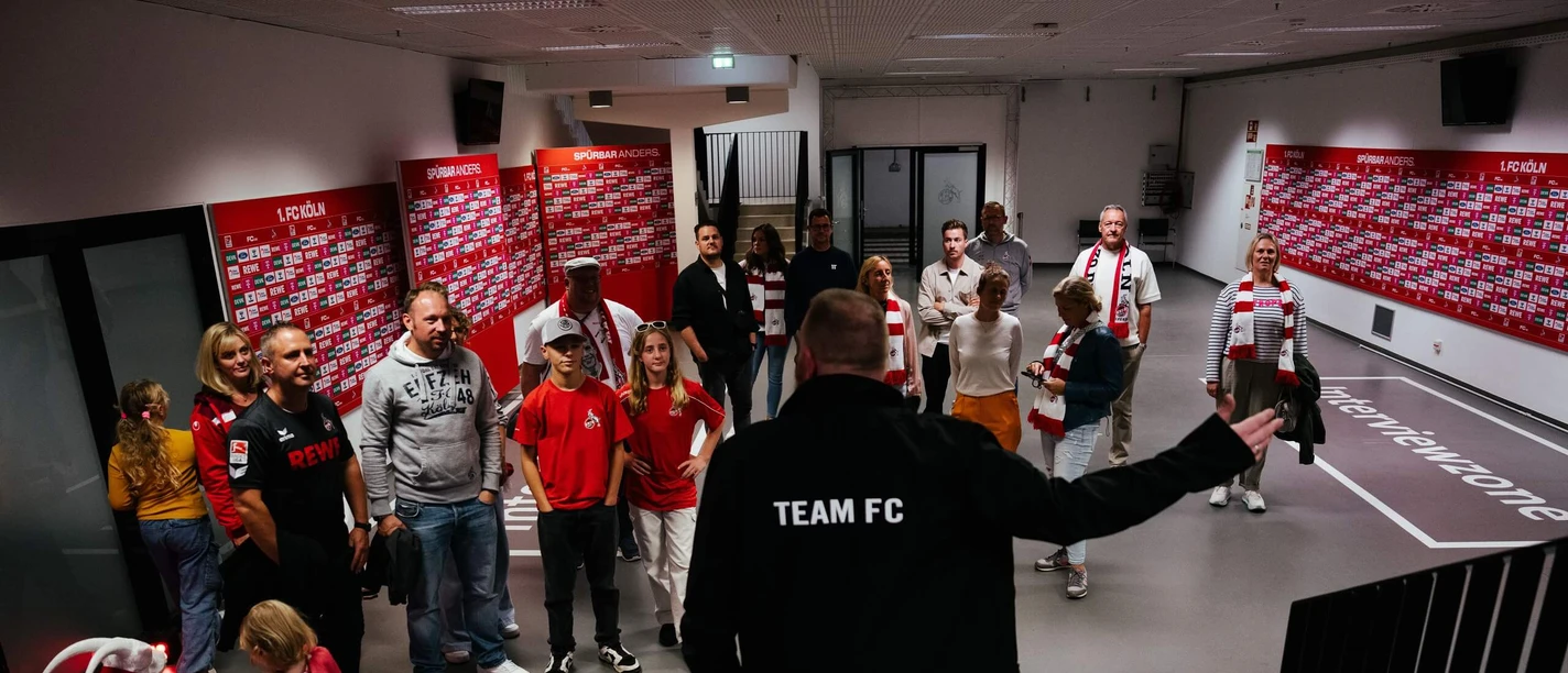 Stadionführung Eine Gruppe steht vor einem Mann und hört aufmerksam zu.