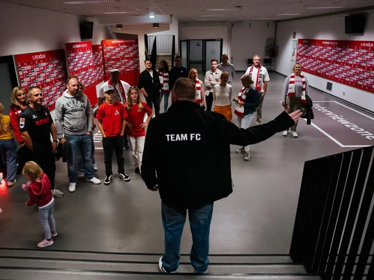 Stadionführung Eine Gruppe steht vor einem Mann und hört aufmerksam zu.A group stands in front of a man and listens attentively.