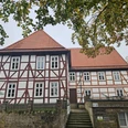 Neuenheerse-Alte Dechanei Fachwerkhaus mit rotem Dach und Treppe im Vordergrund, umgeben von Bäumen.