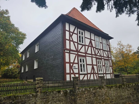 Fachwerkhaus mit rotem Dach hinter Steinmauer an grauem Himmel