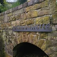 Neuenheerse-Nethequelle Steinbogen mit Metallschrift Nethequelle an einer moosigen Mauer.