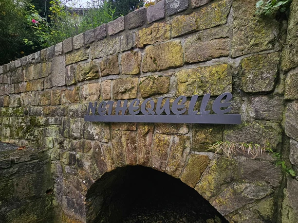Neuenheerse-Nethequelle Steinbogen mit Metallschrift Nethequelle an einer moosigen Mauer.